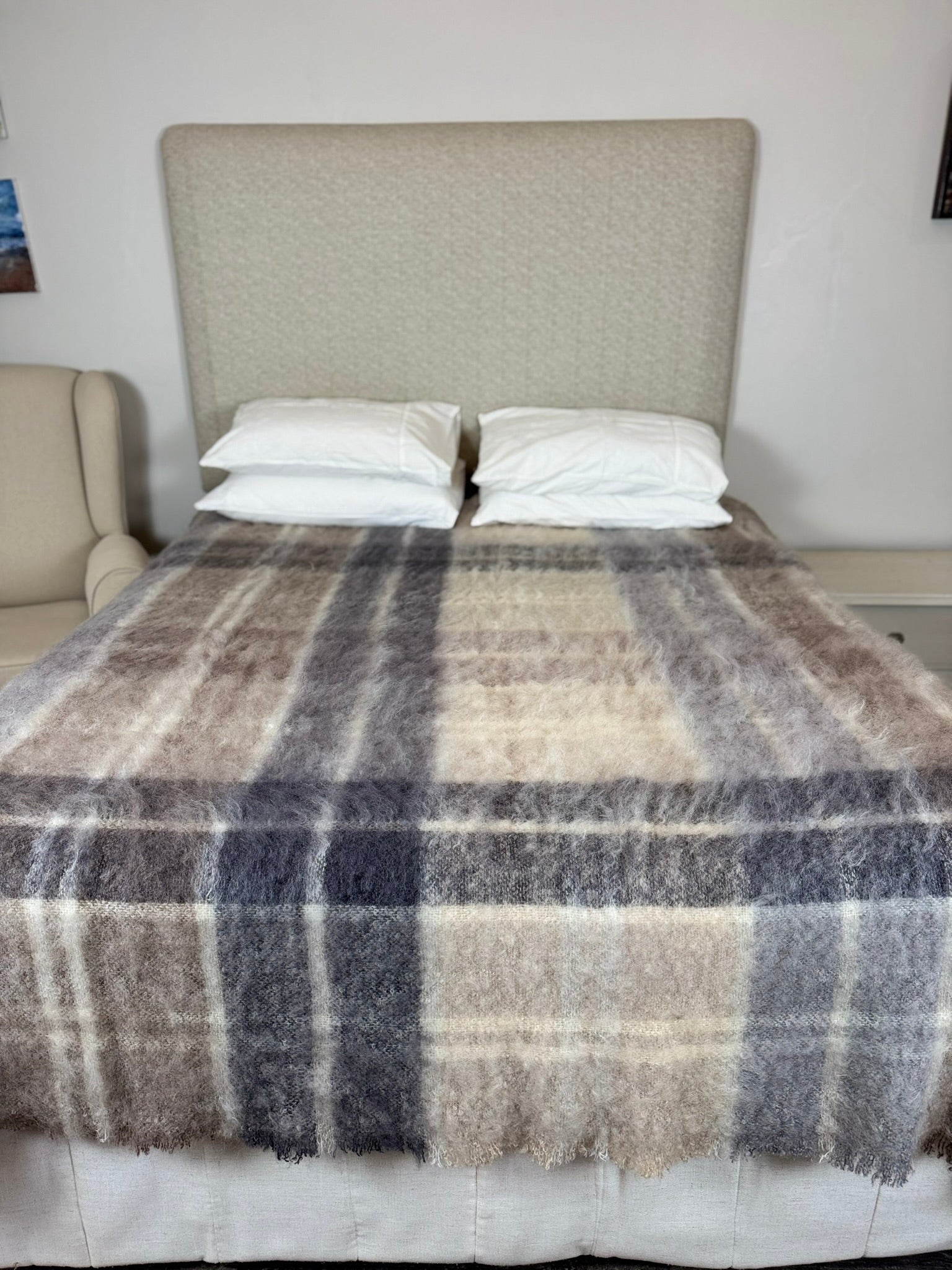 Bed with plaid blanket and pillows against a neutral headboard.